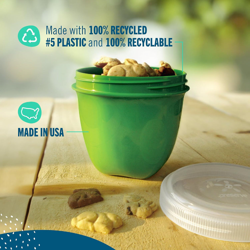 An Apple Green Preserve food storage mini, filled with Annie's bunny snacks, shown on a wooden surface with a clear lid nearby. Text overlays highlight that it is made with 100% recycled #5 plastic and is recyclable, and that it is made in the USA.